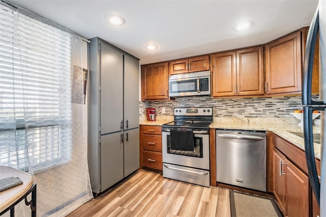 kitchen featuring backsplash, light wood-type flooring, light stone countertops, appliances with stainless steel finishes, and plenty of natural light