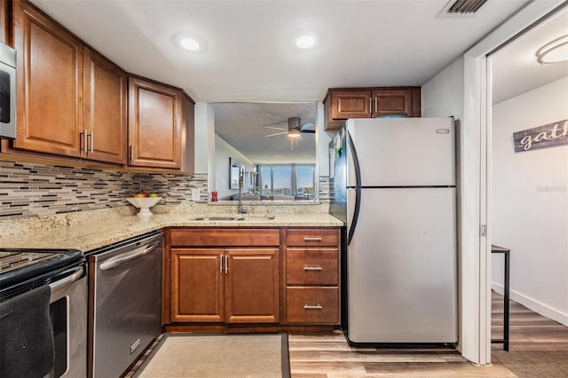 kitchen with sink, light hardwood / wood-style flooring, ceiling fan, light stone countertops, and appliances with stainless steel finishes