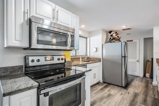 kitchen with white cabinets, sink, stainless steel appliances, and dark stone counters