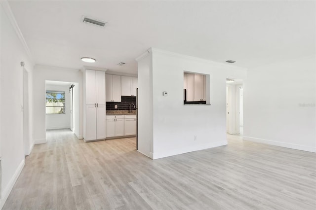 interior space featuring white cabinetry, sink, tasteful backsplash, light hardwood / wood-style flooring, and ornamental molding