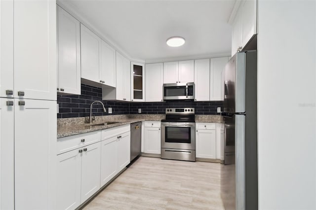 kitchen with stainless steel appliances, sink, dark stone countertops, white cabinets, and light hardwood / wood-style floors