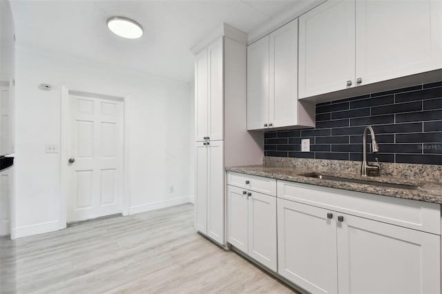 kitchen featuring sink, tasteful backsplash, light hardwood / wood-style flooring, dark stone counters, and white cabinets