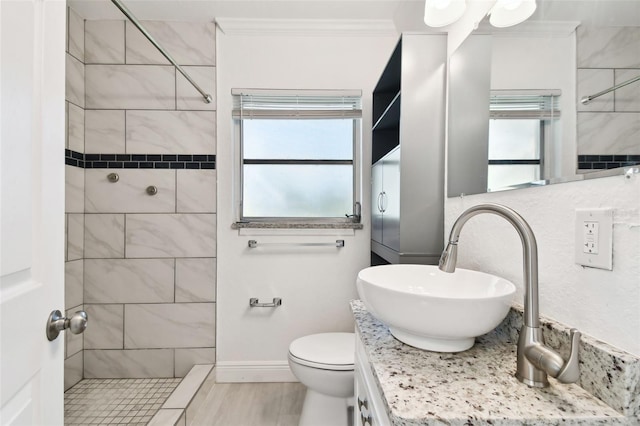 bathroom with toilet, a tile shower, crown molding, and vanity