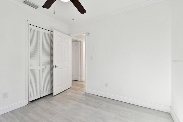 unfurnished bedroom featuring ceiling fan, light wood-type flooring, ornamental molding, and a closet