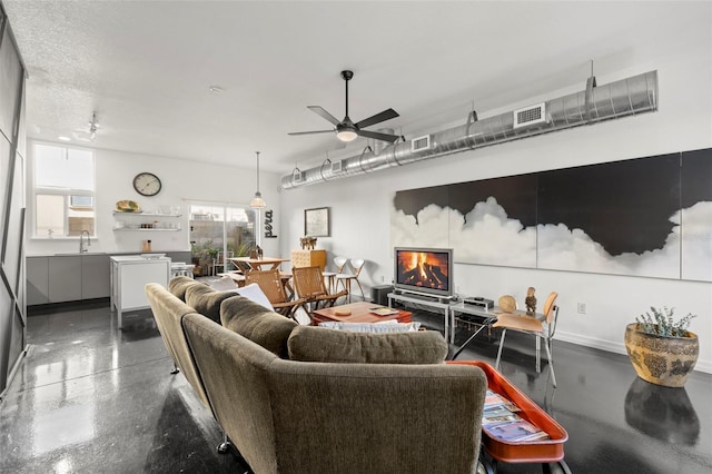 living area with ceiling fan, finished concrete flooring, a warm lit fireplace, and visible vents