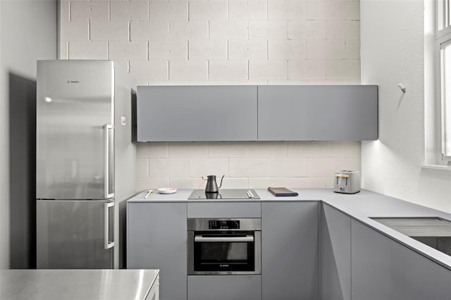 kitchen featuring gray cabinetry, stainless steel appliances, light countertops, backsplash, and modern cabinets