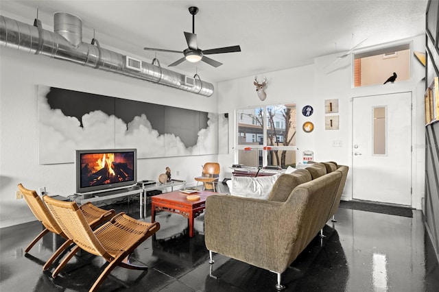 living area with a ceiling fan, a lit fireplace, visible vents, and concrete flooring