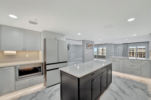 kitchen with stainless steel microwave, backsplash, a kitchen island, white fridge, and light stone counters