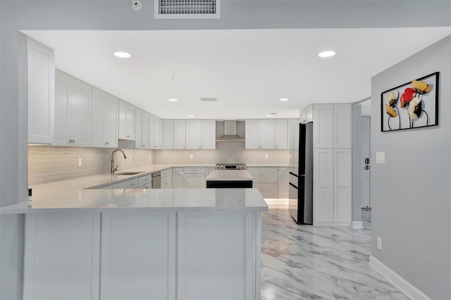 kitchen featuring white cabinets, sink, wall chimney exhaust hood, appliances with stainless steel finishes, and kitchen peninsula