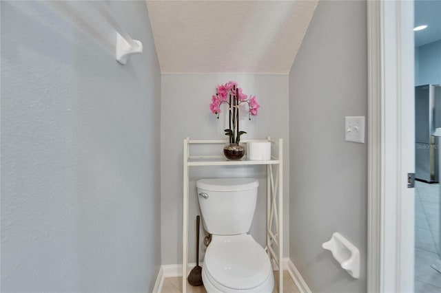 bathroom with toilet, tile patterned flooring, vaulted ceiling, and a textured ceiling