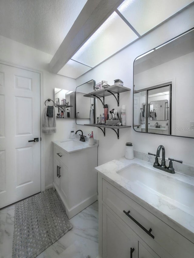 full bath with marble finish floor, a textured ceiling, two vanities, and a sink