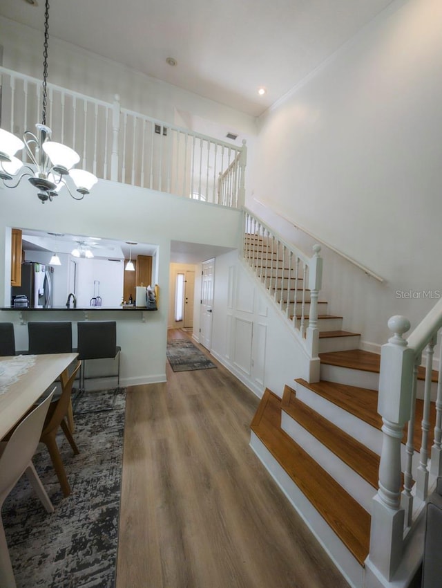 stairway with wood-type flooring, ceiling fan with notable chandelier, and a high ceiling