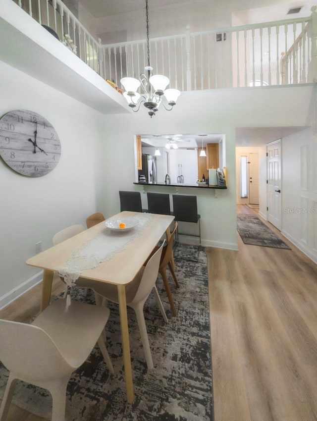 dining space with ceiling fan with notable chandelier, a towering ceiling, and light hardwood / wood-style flooring