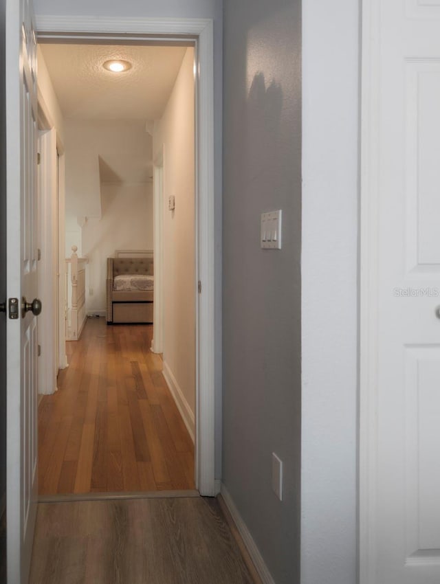 hallway with a textured ceiling, baseboards, and wood finished floors