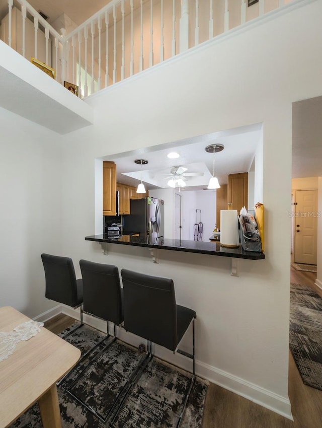 kitchen with kitchen peninsula, a high ceiling, decorative light fixtures, stainless steel fridge with ice dispenser, and a breakfast bar area