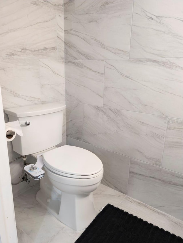 bathroom featuring marble finish floor, toilet, and tile walls