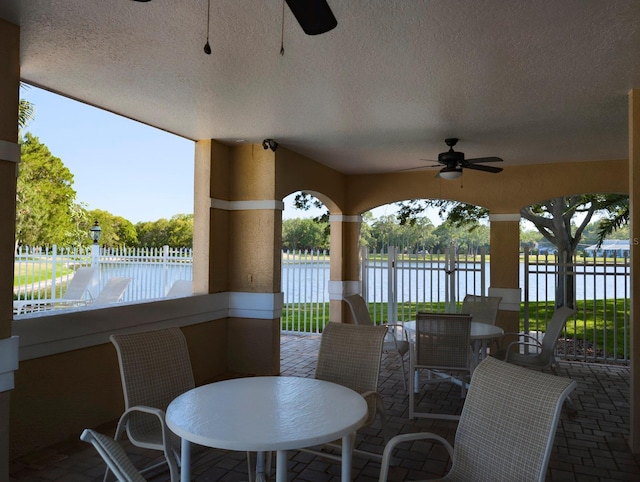 view of patio featuring outdoor dining area, a water view, fence, and a ceiling fan