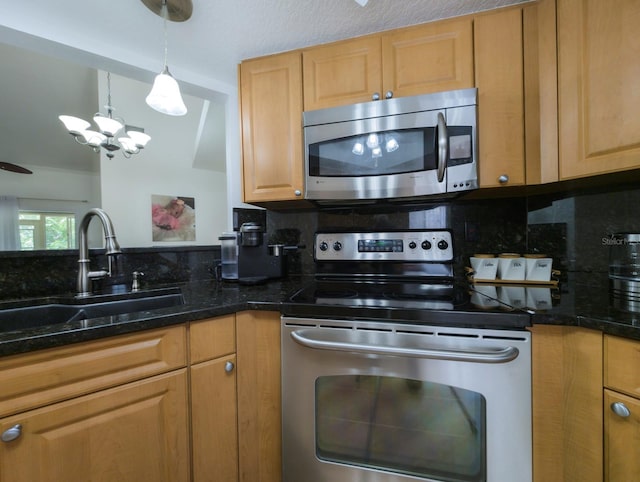 kitchen with pendant lighting, stainless steel appliances, tasteful backsplash, a sink, and dark stone counters