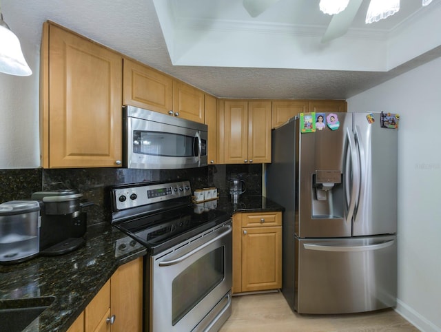 kitchen with ceiling fan, appliances with stainless steel finishes, dark stone countertops, crown molding, and backsplash