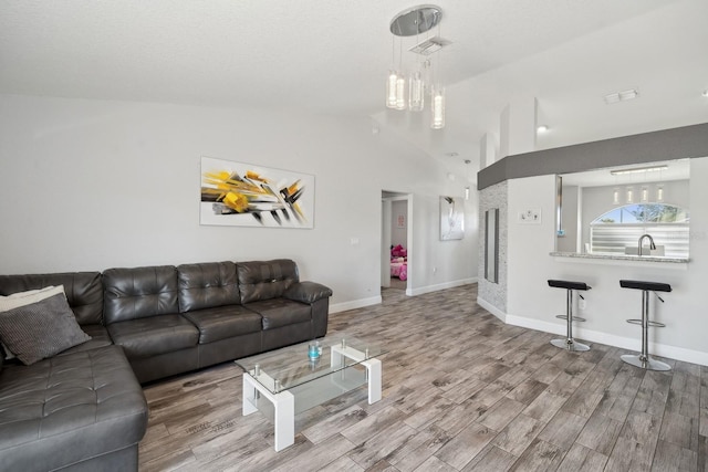 living room with sink, light hardwood / wood-style floors, vaulted ceiling, and an inviting chandelier