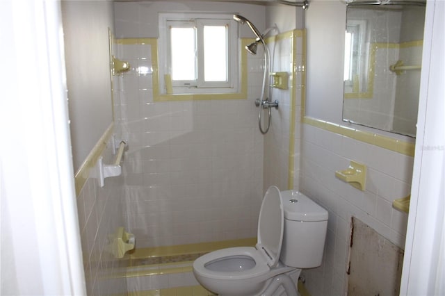 bathroom featuring toilet, a tile shower, and tile walls