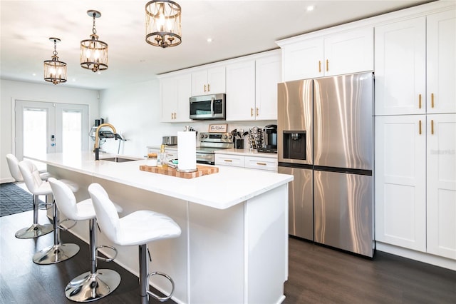 kitchen with pendant lighting, a kitchen island with sink, sink, white cabinetry, and stainless steel appliances