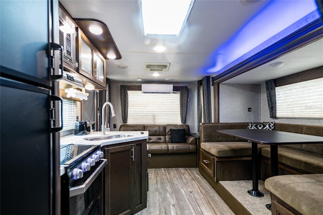 kitchen with dark brown cabinetry, sink, a wall mounted air conditioner, black fridge, and high end stainless steel range