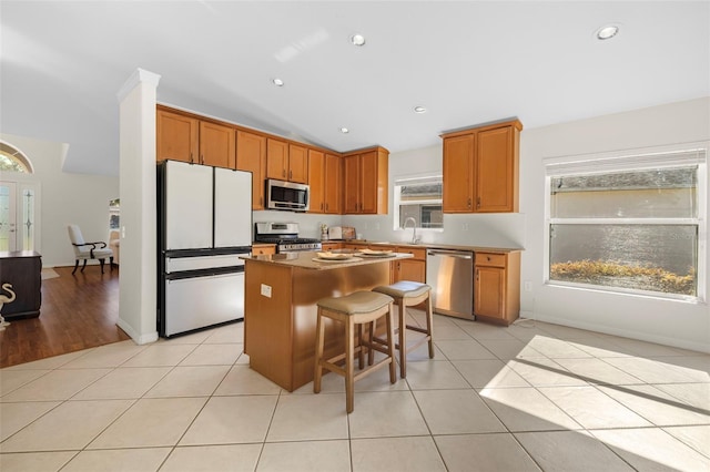 kitchen with stainless steel appliances, a kitchen island, plenty of natural light, light tile patterned flooring, and a breakfast bar area