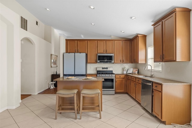 kitchen featuring sink, a center island, light tile patterned floors, a breakfast bar, and appliances with stainless steel finishes