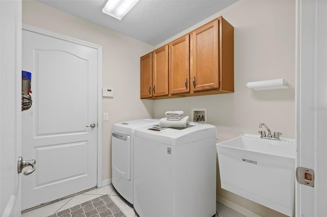 washroom with sink, a textured ceiling, cabinets, light tile patterned floors, and washer and dryer