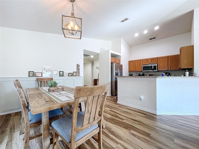 dining space with light hardwood / wood-style floors, lofted ceiling, and an inviting chandelier