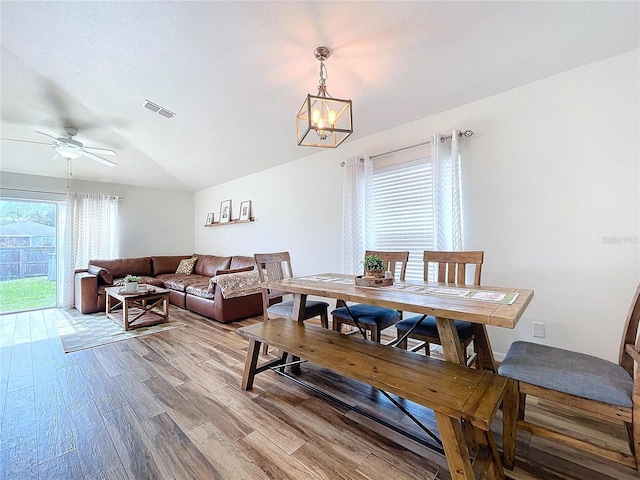 dining space featuring wood-type flooring, ceiling fan with notable chandelier, and lofted ceiling