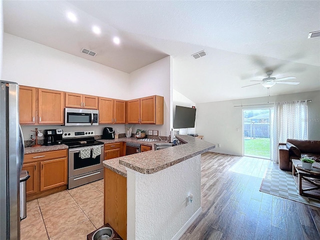 kitchen with kitchen peninsula, stainless steel appliances, ceiling fan, sink, and light hardwood / wood-style floors