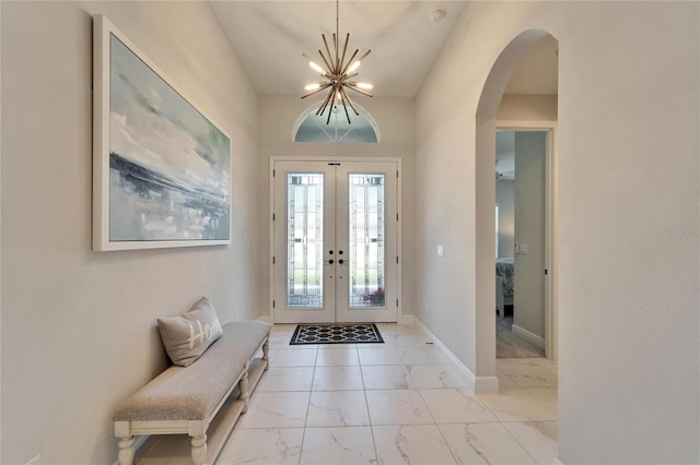 foyer with arched walkways, a chandelier, baseboards, marble finish floor, and french doors