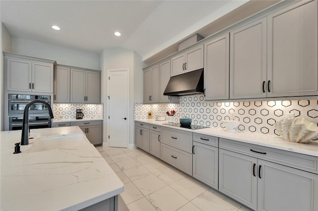 kitchen with marble finish floor, gray cabinets, light stone countertops, under cabinet range hood, and black appliances