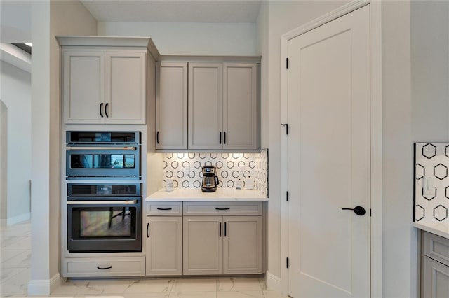 kitchen with double wall oven, marble finish floor, light countertops, gray cabinets, and decorative backsplash