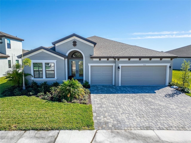 ranch-style home featuring french doors, decorative driveway, stucco siding, a garage, and a front lawn