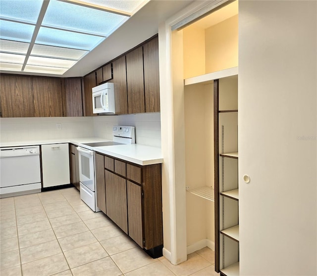 kitchen featuring dark brown cabinetry, light tile patterned flooring, and white appliances