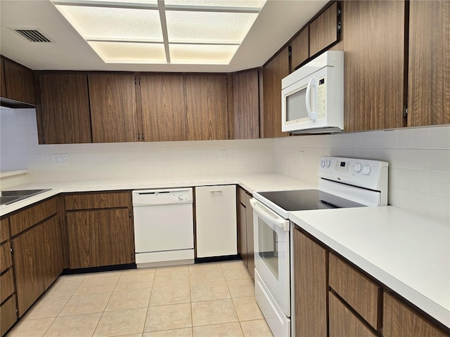 kitchen with light tile patterned floors, white appliances, dark brown cabinets, and backsplash