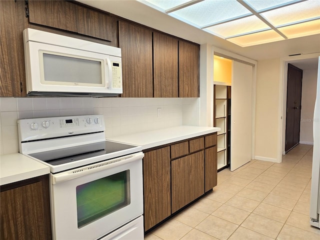 kitchen featuring decorative backsplash, light tile patterned flooring, dark brown cabinets, and white appliances