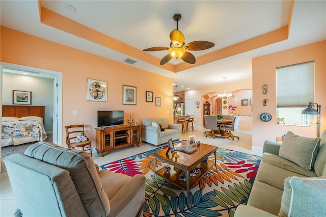 living room featuring light tile patterned floors, ceiling fan with notable chandelier, and a raised ceiling