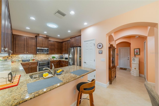 kitchen featuring light stone countertops, stainless steel appliances, kitchen peninsula, decorative backsplash, and a breakfast bar