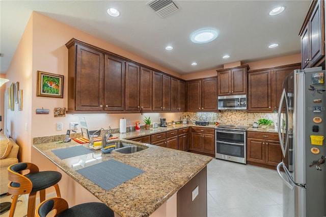 kitchen with sink, stainless steel appliances, light stone counters, kitchen peninsula, and a breakfast bar area