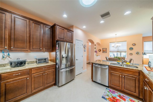 kitchen with appliances with stainless steel finishes, light stone counters, sink, decorative light fixtures, and a notable chandelier