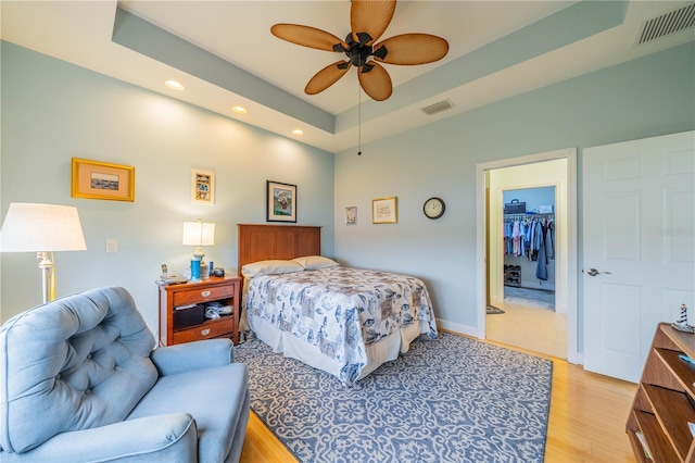 bedroom featuring a raised ceiling, a walk in closet, ceiling fan, light hardwood / wood-style floors, and a closet