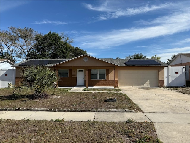 ranch-style house with roof mounted solar panels, brick siding, driveway, and an attached garage