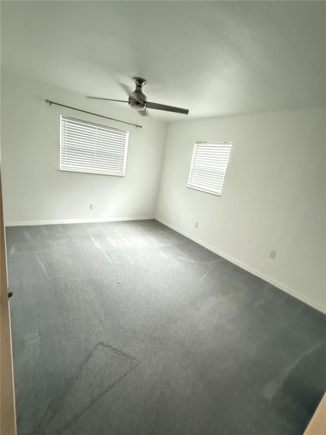 empty room with ceiling fan, dark carpet, and baseboards