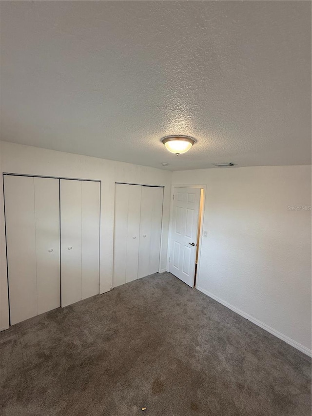 unfurnished bedroom featuring carpet floors, a textured ceiling, and multiple closets