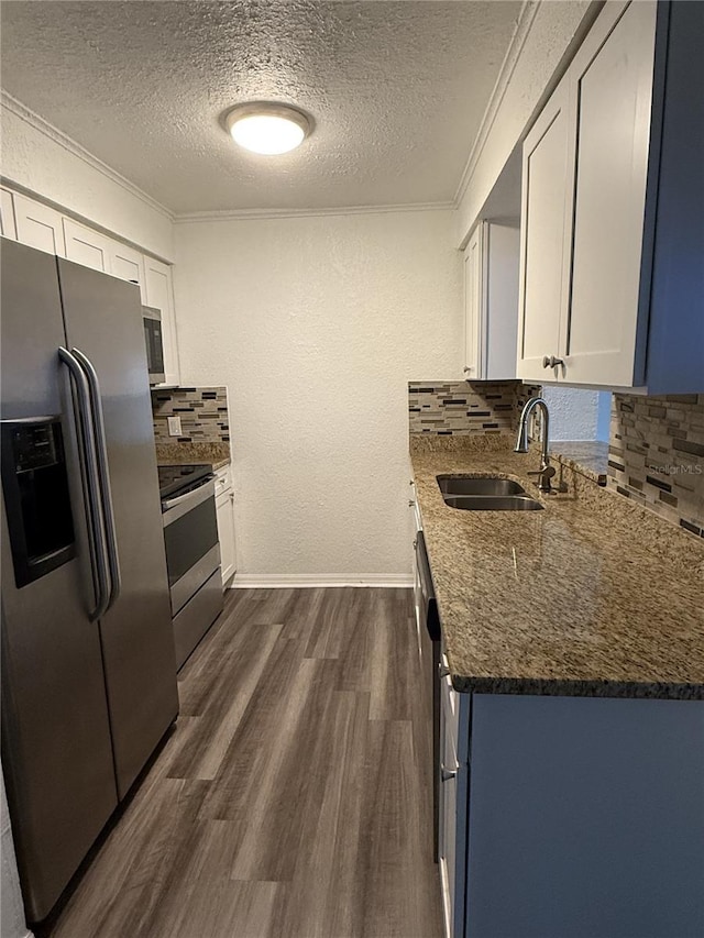 kitchen featuring stainless steel appliances, a sink, ornamental molding, dark stone counters, and dark wood finished floors