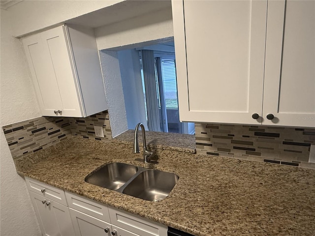 kitchen featuring decorative backsplash, white cabinets, a textured wall, stone counters, and a sink